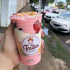 a hand holding up a pink ice cream sundae with toppings on the top