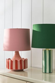 two lamps sitting on top of a table next to each other, one pink and the other green