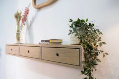 a wooden shelf with some books and plants on it next to a wall mounted clock