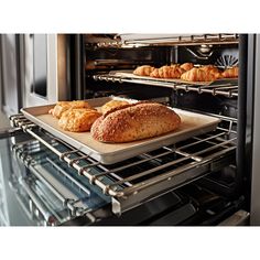 two loaves of bread sit on a tray in front of an open oven door