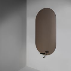 an oval mirror mounted to the side of a wall next to a black hook on a white wall