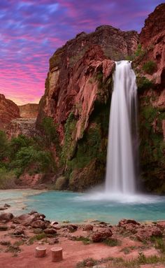 a large waterfall is in the middle of a body of water with red rocks surrounding it