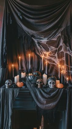 a mantle with candles and skulls on it in front of a black drapeed curtain