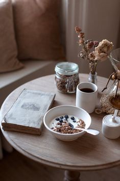 a wooden table topped with two bowls of cereal and coffee next to a vase filled with flowers