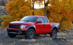 a red truck is parked in the grass near some trees with yellow and orange leaves