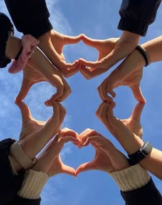 several hands making a heart shape with their fingers in the air against a blue sky