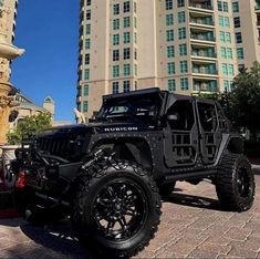 a black jeep parked in front of a tall building on a brick road next to a fountain