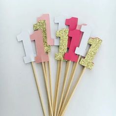 there are some pink and gold cake toppers on sticks with the number one in them