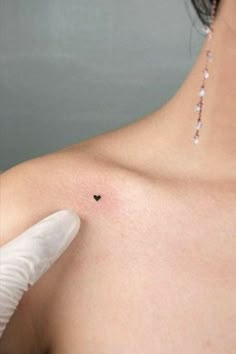 a woman's breast with a small heart tattoo on her left shoulder and a white glove