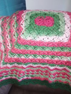 a crocheted blanket with a heart on it sitting on a couch next to a pillow