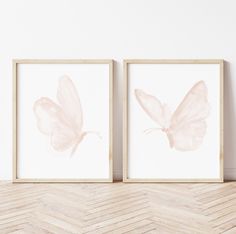 two framed pictures with pink butterflies in them on a wooden floor next to a white wall