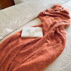 an orange blanket on top of a bed next to a book