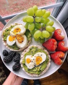 a person holding a plate with fruit and crackers on it next to some grapes