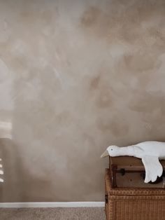 a white bird sitting on top of a wooden box in front of a gray wall