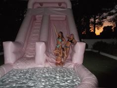 three women in swimsuits are standing on an inflatable slide at night