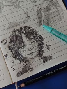 a notebook with some drawings on it next to a blue pen and eraser pens