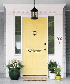 a yellow door with the words welcome on it and potted plants next to it