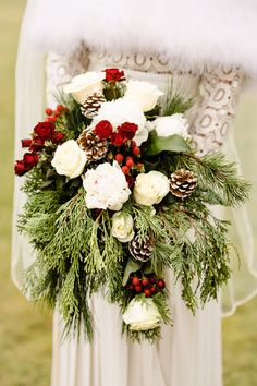 a bridal holding a bouquet of flowers and pine cones in her hands with fur on the back