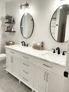 a white bathroom with two round mirrors above the sinks and toilet in front of it