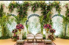 an elaborately decorated room with two chairs and flowers on the wall behind them, surrounded by greenery