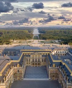 an aerial view of a large building in the middle of a field with trees and clouds