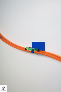 an orange and blue toy car on top of a long plastic track that is connected to a white wall