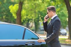 a man in a suit is talking on his cell phone next to a black car