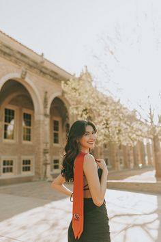 a woman wearing a black dress and an orange neck tie standing in front of a building