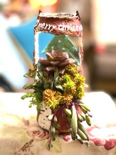 an arrangement of flowers in a vase sitting on a table with a sign that says merry christmas