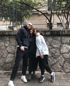 three people standing next to each other in front of a stone wall