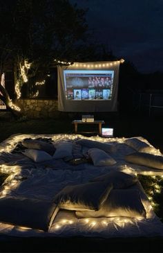 an outdoor movie screen is lit up at night with lights on the ground and pillows all around it