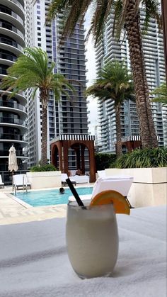 a cocktail cup with an orange slice in it sitting on the ground next to a swimming pool