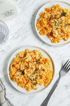 two white plates topped with scrambled eggs next to a fork and glass of water on a marble table