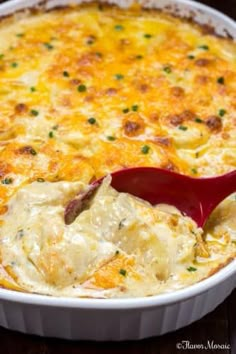 a casserole dish filled with potatoes and cheese being spooned into the casserole