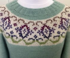 a green sweater with multicolored designs on the front and back, sitting on a mannequin head