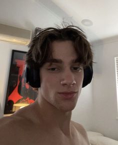 a shirtless man wearing headphones in his bedroom