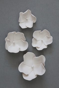 four white flower shaped dishes sitting on top of a gray tableclothed surface, with three petals in the center