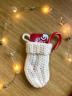 a white knitted stocking with a red handle on a wooden table surrounded by christmas lights