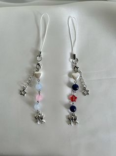 two pairs of earrings with charms hanging from them on a white cloth covered bed sheet