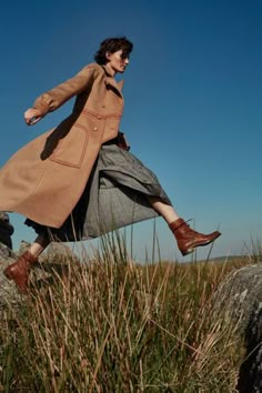 a woman is jumping in the air over some rocks and grass with her legs spread out