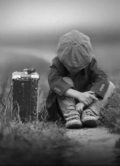 a little boy sitting on top of a grass covered field next to an old suitcase