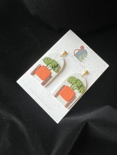 a pair of earrings with green and orange designs on them sitting on a black cloth