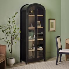 a room with green walls and a black china cabinet next to a white chair in the corner