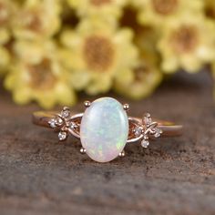 a white opal and diamond ring sitting on top of a table next to flowers