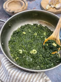 a pan filled with spinach on top of a table next to wooden spoons