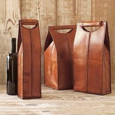 three leather wine bags and a bottle on a wooden table