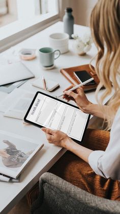 a woman sitting at a table with a tablet computer and papers on top of it