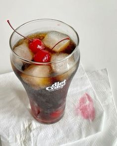 a glass filled with ice and cherries on top of a napkin