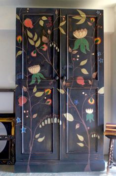 an armoire painted with flowers and leaves on the wall next to a stool in a room