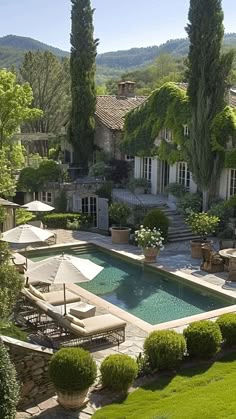 an outdoor pool surrounded by lawn chairs and umbrellas in front of a large house